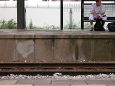 station waiting person man walls concrete rail trainstation rails bench bag bags human humanoid bottle